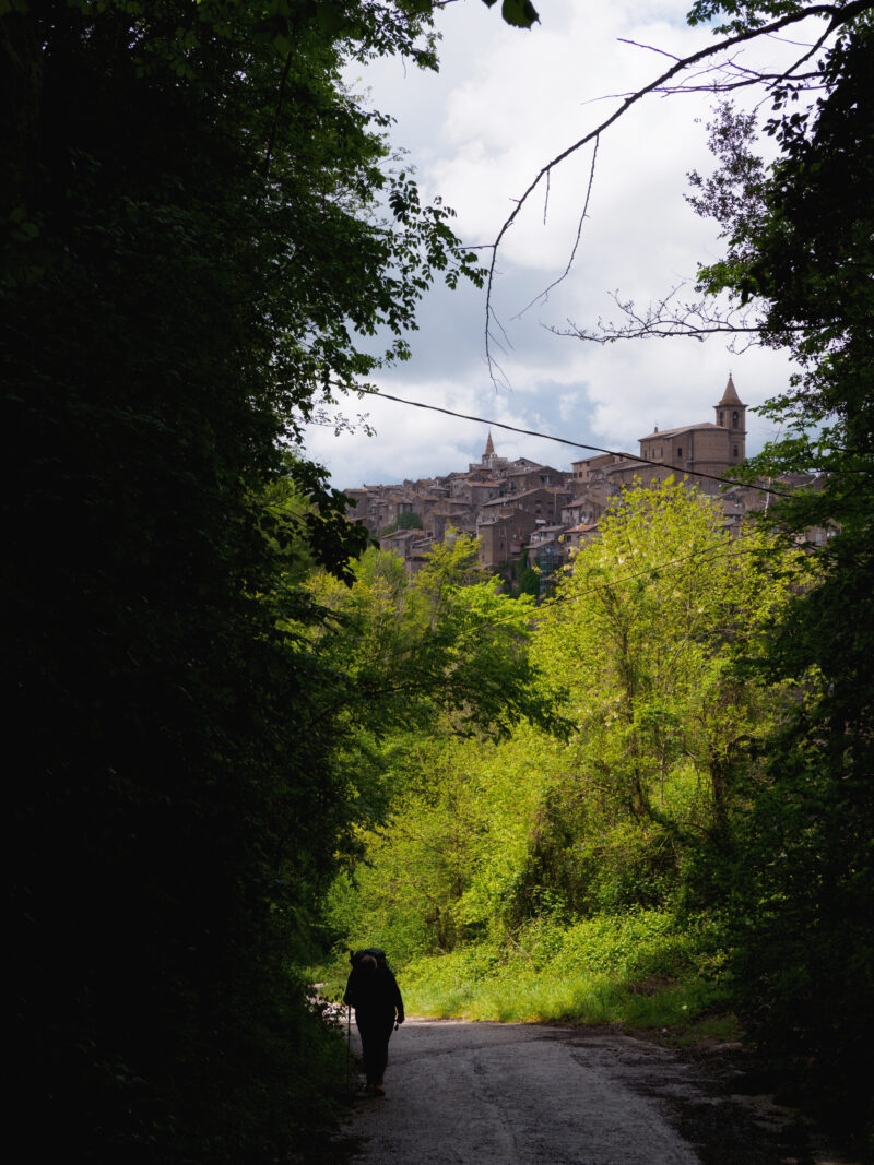 Pellegrino solitario con bastone che si allontanadal borgo di capranica