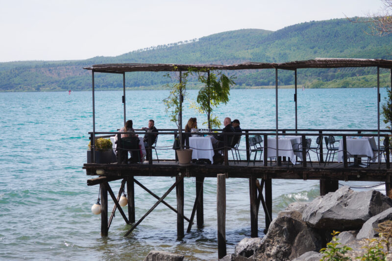 Ristorante su palafitte sull'acqua del lago con colline boscose sullo sfondo a Trevignano Romano