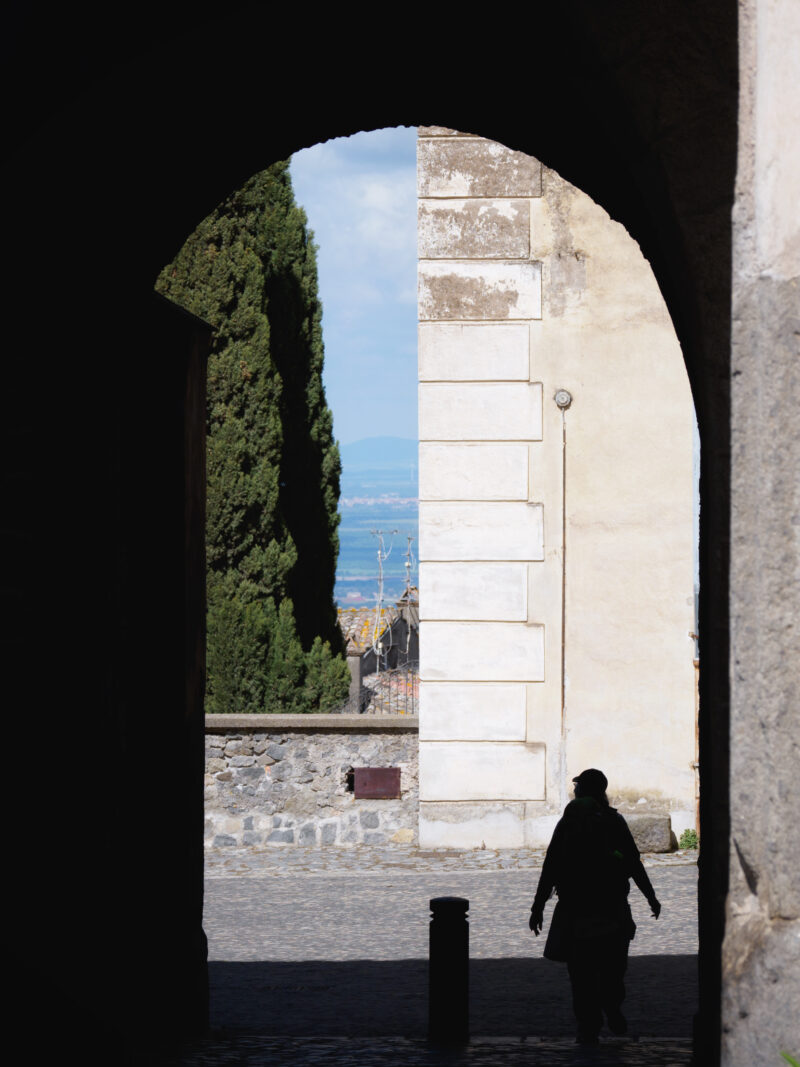 Silhouette di un pellegrino della via francigena sotto un arco in pietra con cielo azzurro