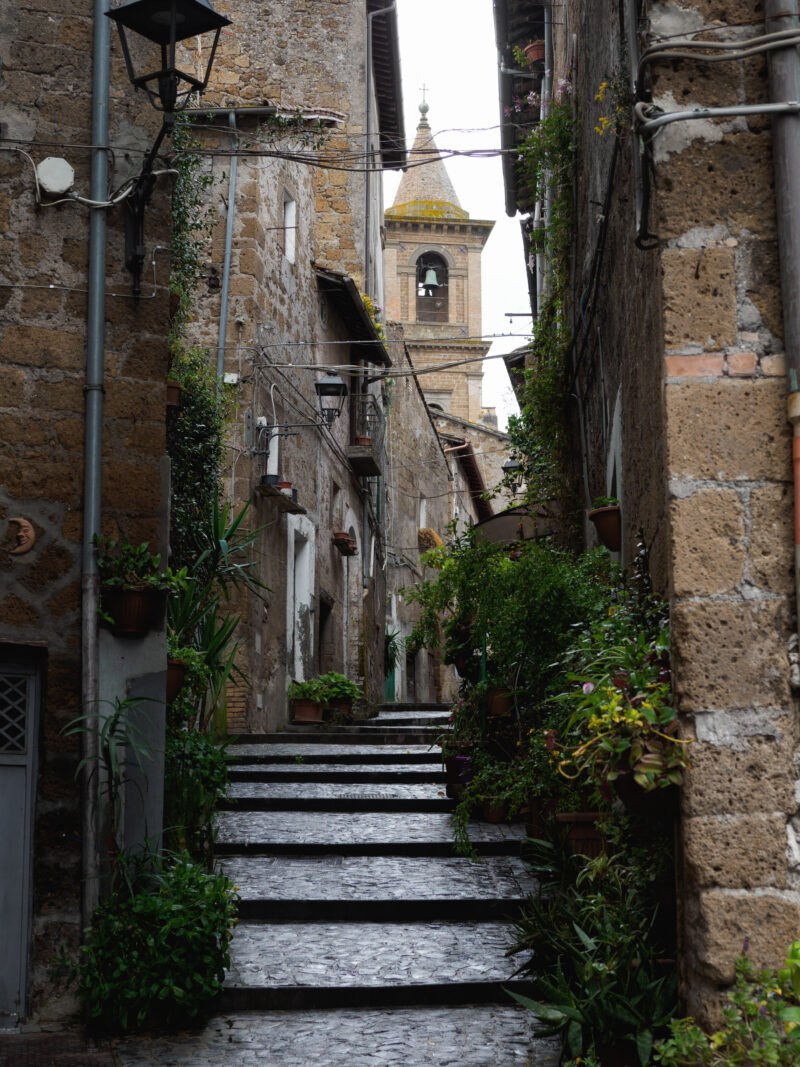 Vicolo con scalinata in pietra e campanile sullo sfondo del borgo mediovale di Capranica