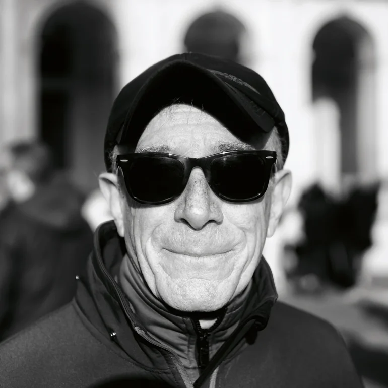 Uomo con occhiali e cappello con un sorriso a bocca chiusa trattenuto