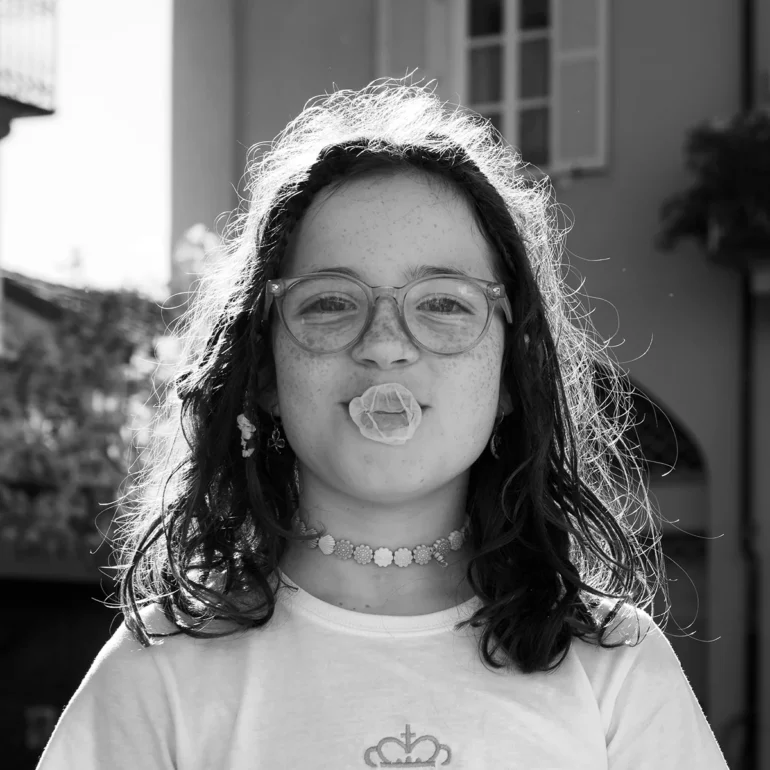 Bambina che sorride con occhi mentre scoppia una bolla fatta con gomma da masticare in faccia