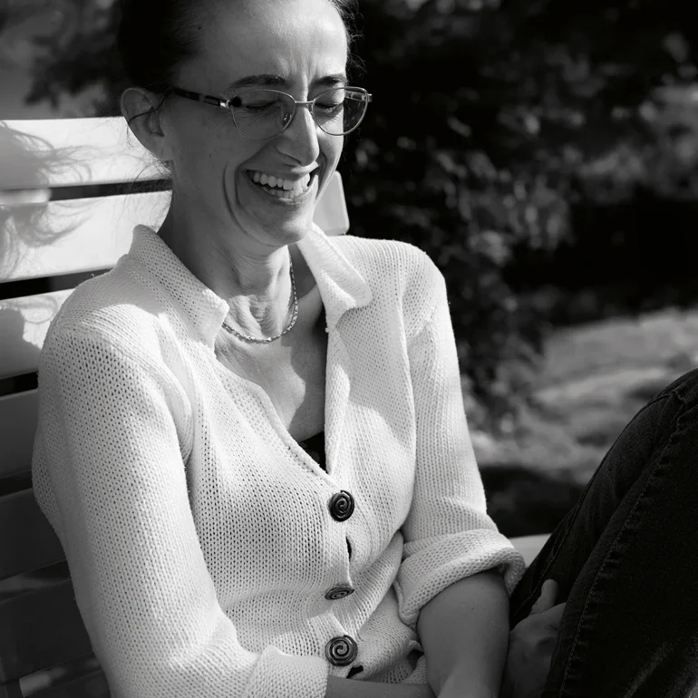 Donna dal maglione bianco che ride di gusto seduta su una panchina