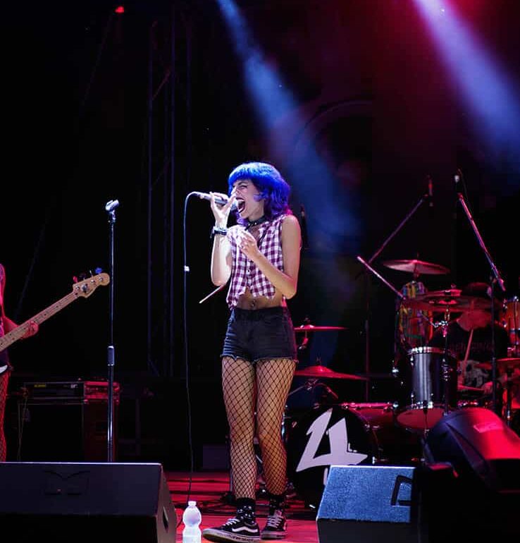 Scatto di una ragazza che canta sul palco di un concerto rock, luci di scena dinamiche e atmosfera carica di energia