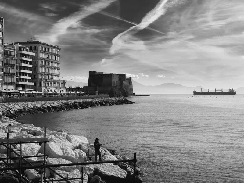 Foto in bianco e nero del porto di Napoli con sullo sfondo grande nave e in primo piano un pescatore