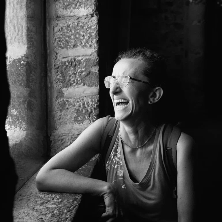 Donna che ride a crepa pelle alla finestra di una chiesa con luce soffusa vestita con cannottiera.