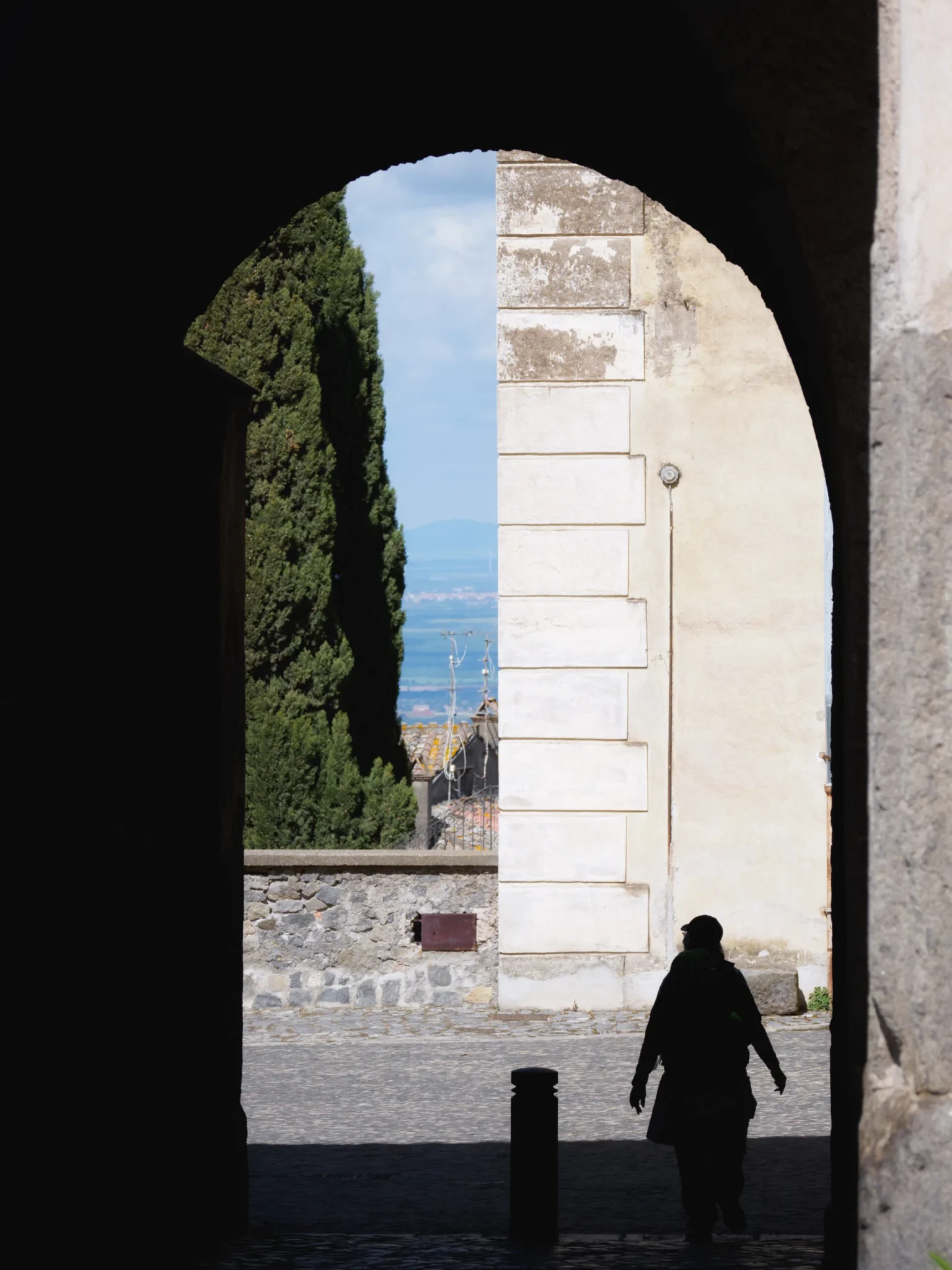Silhouette di un pellegrino della via Francigena sotto un arco in pietra con cielo azzurro